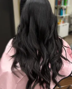 Long dark hair with soft layers and waves, client in a pink cape